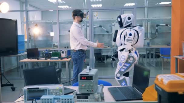 An engineer in augmented reality glasses and a robot are shaking hands — Stock Video