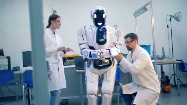 Uma mulher e um homem engenheiros estão reparando um cyborg com ferramentas — Vídeo de Stock