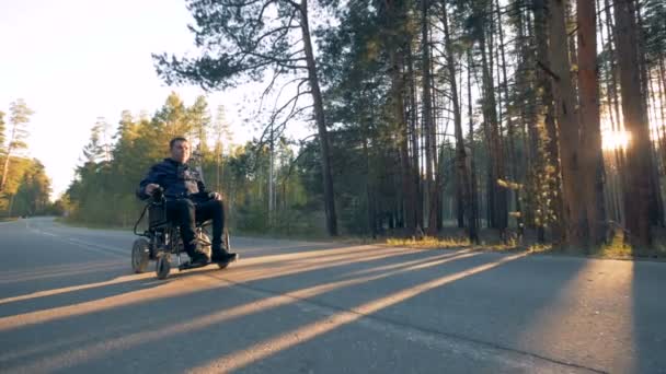 El hombre parapléjico se está moviendo por la carretera en su silla de ruedas motorizada en el bosque — Vídeo de stock