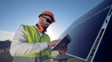 Erkek mühendis bir tablet bilgisayar ile bir güneş pili yakınındaki bir çatı üzerinde duruyor 