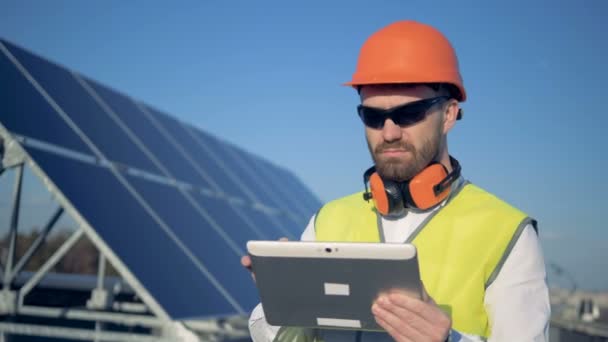 Construtor masculino está de pé ao lado do painel solar e trabalhando. Painéis solares coletando luz solar . — Vídeo de Stock