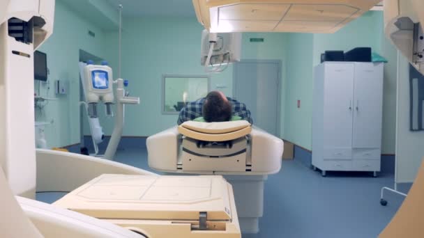 Людина лежить в магнітному резонансному пристрої зображення. Чоловік лежить у лікарняній кімнаті з робочим CAT-сканером — стокове відео