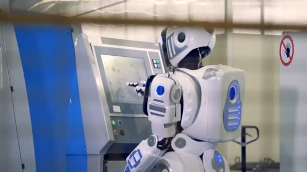 Baksidan vy av en människoliknande robot trycka på olika knappar på sensorn skärmen på en industriella fabriksgolvet. — Stockvideo