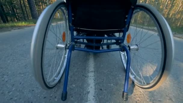 Vista posterior de una silla de ruedas de entrenamiento en movimiento con un hombre discapacitado en ella — Vídeos de Stock