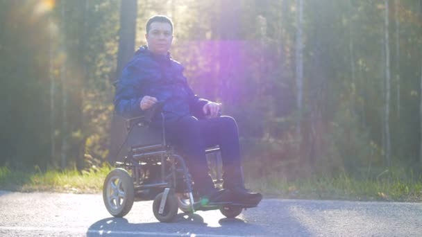 Une personne paraplégique est assise dans un fauteuil roulant à l'extérieur et regarde dans la caméra — Video