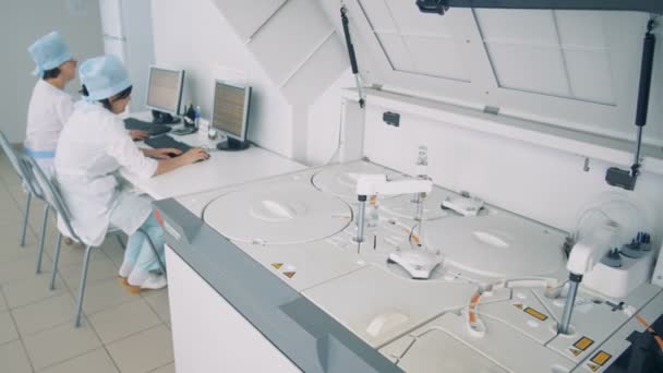 Two doctors sit at computers, while laboratory testing equipment is in process. — Stock Video