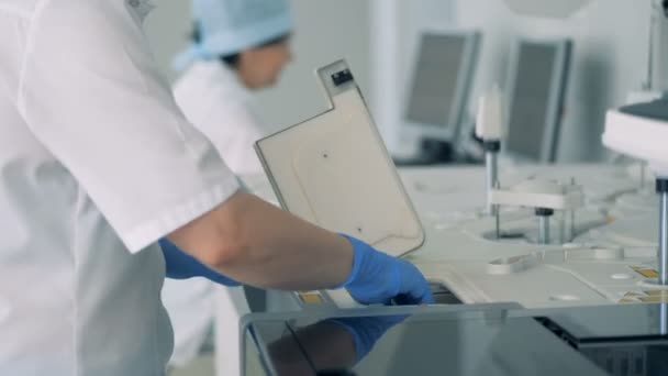 Медсестра забирает образцы бутылок после испытаний специальной машины в современной лаборатории . — стоковое видео