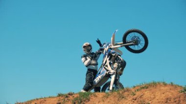 Motosikletçi bisikletini dikey tutarak ve bir parmak hareketi gösterilen