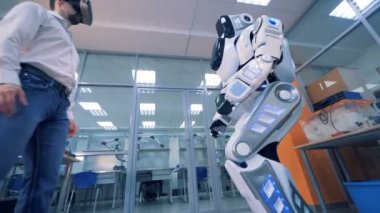 VR oyun kavramı. Vr gözlüklü bir adam el sallıyor bir robot, alttan görünüm.