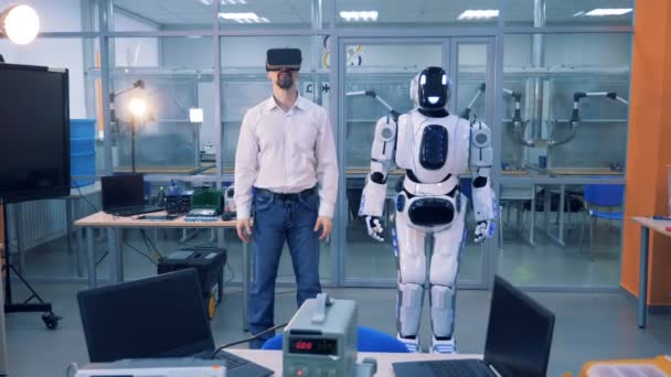 Ένας άνθρωπος σε Vr γυαλιά και ένα cyborg στέκονται σε ένα δωμάτιο. VR gaming έννοια. — Αρχείο Βίντεο