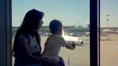 Havaalanında uçaklar için arayan anne ve oğlu oturmak.