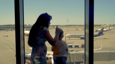 Bir kadın ve bir çocuk bekleyen bir yolculuk için Havalimanı pencereden bakmak.