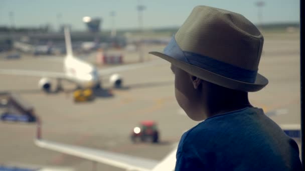 Un chico mira la pista de aterrizaje en un aeropuerto esperando un viaje, de cerca . — Vídeos de Stock