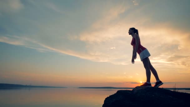 Ein Mädchen nimmt eine Pose ein, während es vor dem Hintergrund des Sonnenuntergangs trainiert. 4k. — Stockvideo