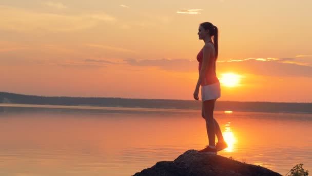 Una mujer estira su pierna sobre un fondo al atardecer . — Vídeos de Stock