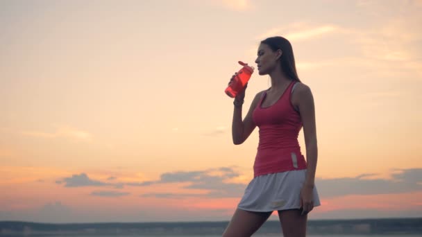 A woman drinks from a red plastic bottle, close up. — Stock Video