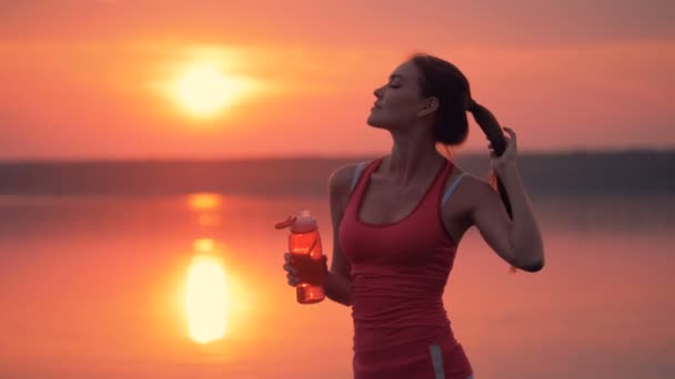 Prachtige jonge vrouw is haar haren streelt en drinken uit een fles — Stockvideo