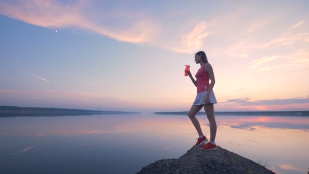 Lenyűgöző kilátás nyílik a sunrise tó egy fiatal nő, ivás közelében — Stock videók