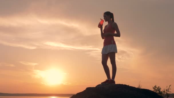 Mujer joven en uniforme deportivo está de pie sobre una roca y beber — Vídeos de Stock