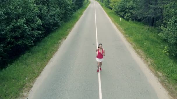Der Fokus rückt weg von einer schlanken hübschen Frau, die in der Gasse joggt. Antenne. — Stockvideo