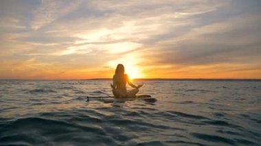 Sörf tahtası üzerinde meditasyon süreci. Kadın sörfçü onun gemide su üzerinde yüzen sırasında derin derin düşünür..