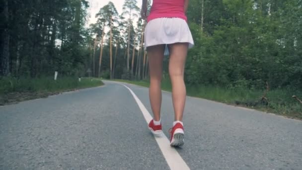 Bosque de carretera con un joven ladys piernas trotando a lo largo de ella. Steadicam, cámara lenta . — Vídeo de stock