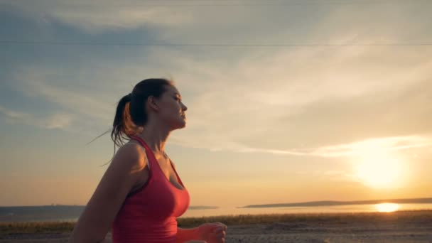 Attraktiv dam jogging längs kusten i solnedgången — Stockvideo