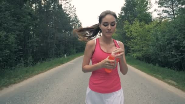 Attraktiv ung dam öppnar en flaska och dricka medan joggning. Hälsosamt smal ung idrottskvinna kör. — Stockvideo