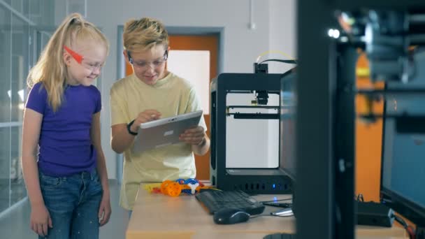 Os colegas de classe olham para um tablet enquanto trabalham com uma impressora 3D em um laboratório. 4K . — Vídeo de Stock