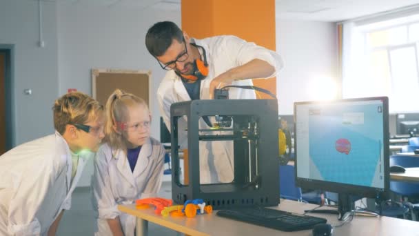 Niños y un maestro de escuela trabajan con una impresora 3D en un laboratorio, de cerca . — Vídeos de Stock