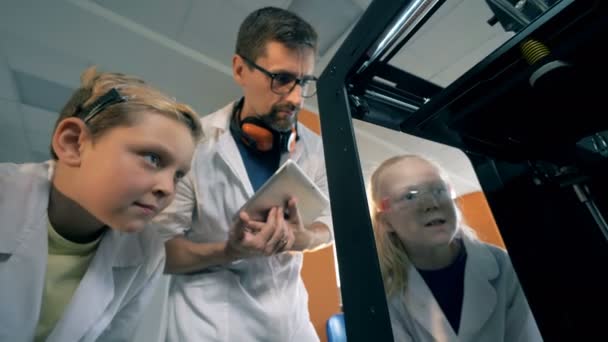 Los niños y un maestro observan una impresora 3D en un laboratorio escolar. 4K . — Vídeo de stock