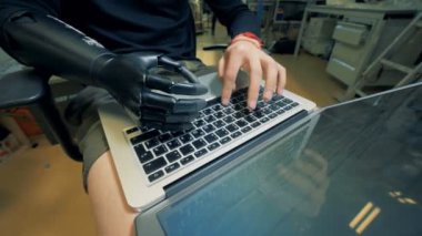 Dizlerinin üzerinde bir dizüstü bilgisayarda bir robot el türleriyle çalışan adam. 4k.