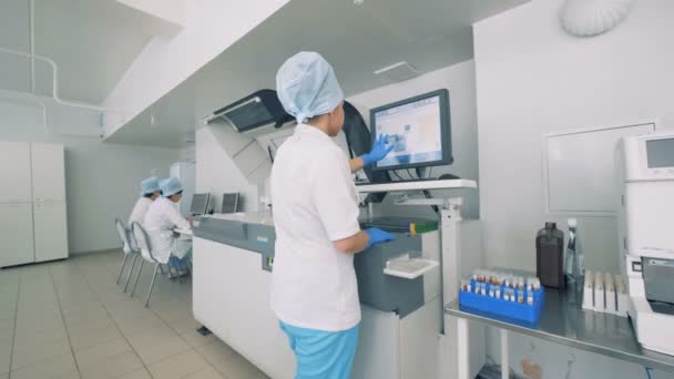 Лабораторное учреждение с женщиной-лаборантом, работающей с сенсорным экраном на автоматическом фармацевтическом оборудовании . — стоковое видео