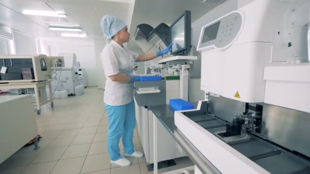 Especialista em pé perto do analisador bioquímico e trabalhando com um equipamento farmacêutico automático . — Vídeo de Stock