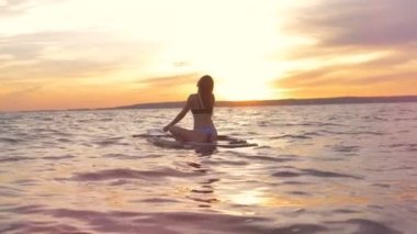 Günbatımı manzara muhteşem bir kadınla bir paddleboard üzerinde oturuyor. Gevşeme kavramı.
