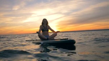 Lotus poz gülümseyen kadın onu paddleboard üzerinde sürüklenen. Gevşeme kavramı.