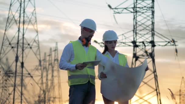 Engenheiros em hardhat trabalhando com projeto de concessão perto de linha de alta tensão, linha de tensão, linha de energia de tensão . — Vídeo de Stock