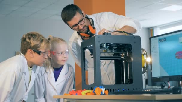 El asociado de laboratorio está demostrando el proceso de trabajo de una impresora 3D a los niños — Vídeo de stock