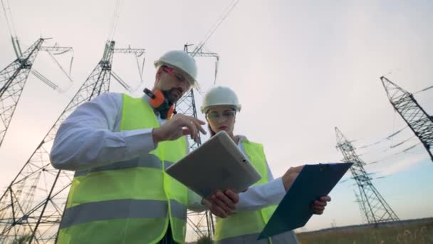 Электрики мужского и женского пола обсуждают электрооборудование вблизи линии электропередач . — стоковое видео