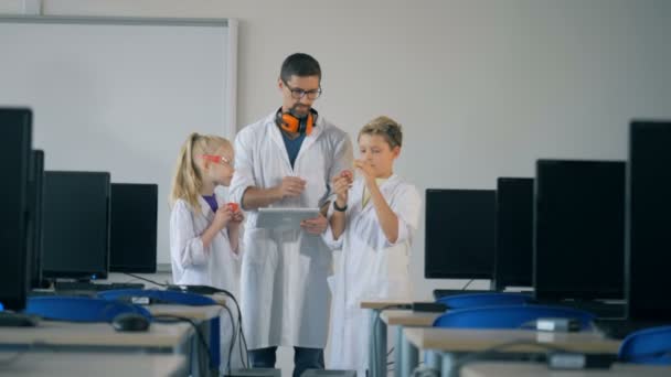 Hombre trabajador de laboratorio y dos niños están de pie en una sala de computadoras y observando los detalles de repuesto — Vídeos de Stock