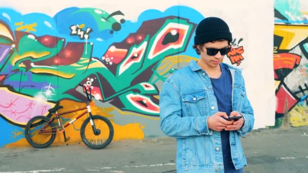 Giovani tipi di adolescenti caucasici eleganti su uno smartphone su uno sfondo di bicicletta, da vicino . — Video Stock