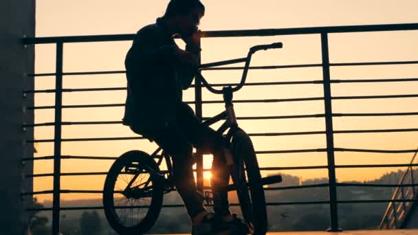 Egy férfi ül a naplemente háttér kerékpárt. Sziluettjét. tinédzser aktív.. — Stock videók