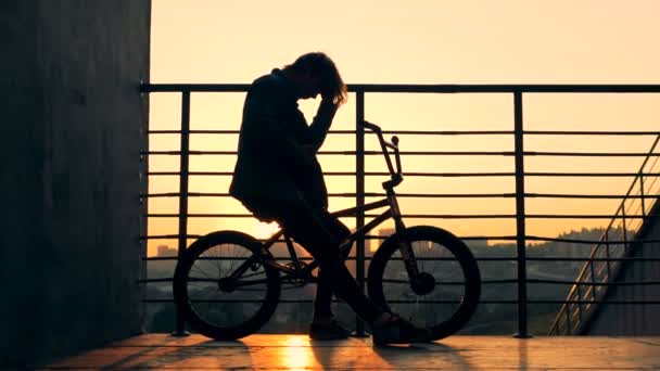 Una persona se sienta en una bicicleta sobre un fondo al atardecer, de cerca . — Vídeos de Stock