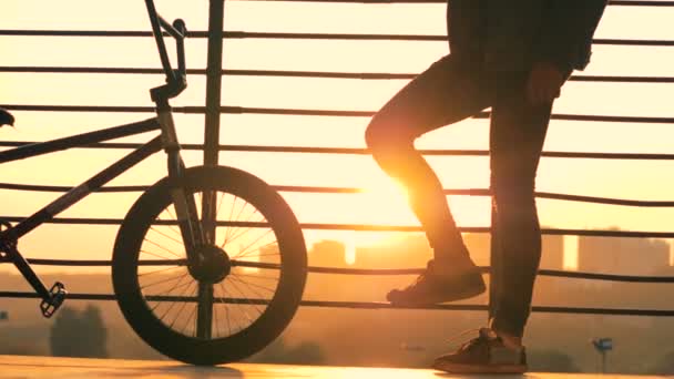 El hombre se para con una bicicleta sobre un fondo al atardecer, de cerca . — Vídeo de stock