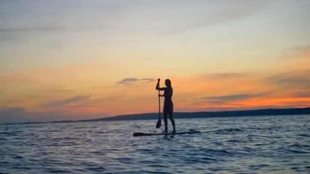 Ηλιοβασίλεμα τοπίο με μια γυναίκα paddleboarding μέσω ανοιχτής θαλάσσης. Καλοκαιρινές διακοπές ταξίδια έννοια. — Αρχείο Βίντεο