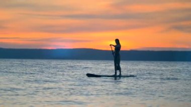 Günbatımı manzara muhteşem bir hanımla bir paddleboard üzerinde yüzer. Özgürlük kavramı.