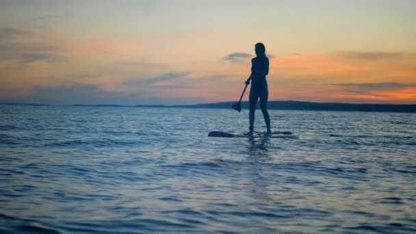 Pintoresca puesta de sol con una silueta femenina navegando de un paddleboard. Concepto de estilo activo . — Vídeos de Stock