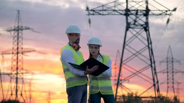 Engineers in uniform working with a laptop near transmission lines. — Stock Video