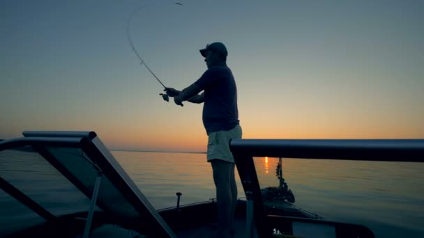 Pescador masculino está lanzando una caña de pescar en un lago iluminado por el sol — Vídeo de stock
