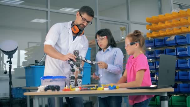 Salle de jeux d'ingénierie avec deux adolescents et un travailleur masculin apprenant à connaître un robot jouet — Video